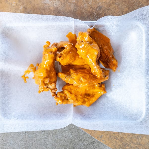 Top-down view of several buffalo chicken wings coated in orange sauce, served in a white paper-lined tray.