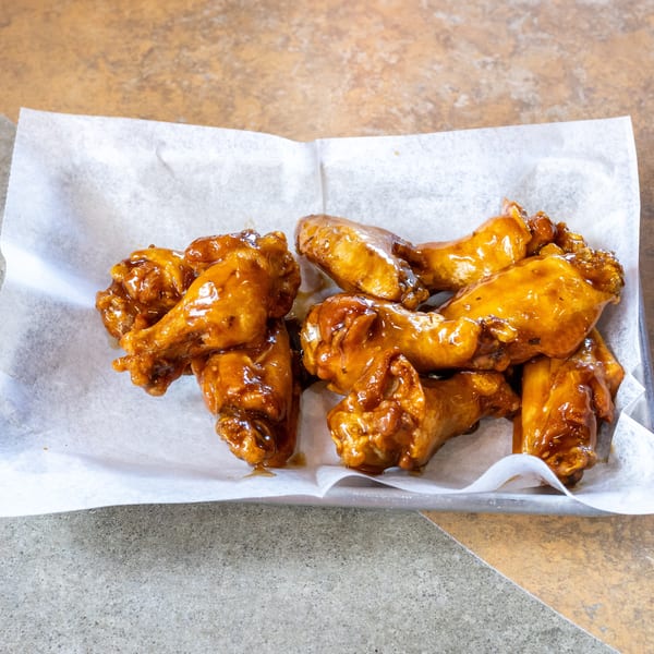 A metal tray lined with white parchment paper holds several glistening, saucy chicken wings.
