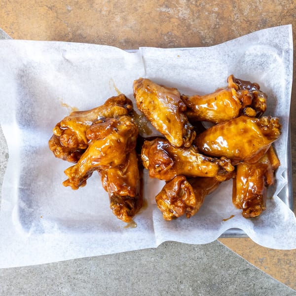 A tray of golden-brown chicken wings coated in a glistening, sticky sauce on white parchment paper.