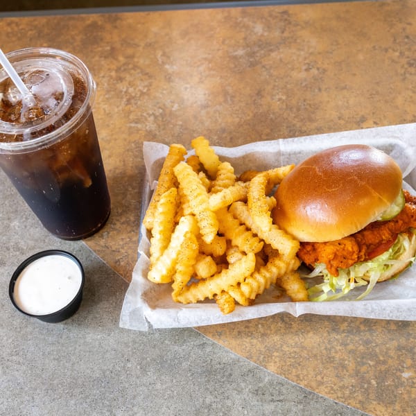 Spicy fried chicken sandwich with crinkle-cut fries, a side of ranch, and a soda.