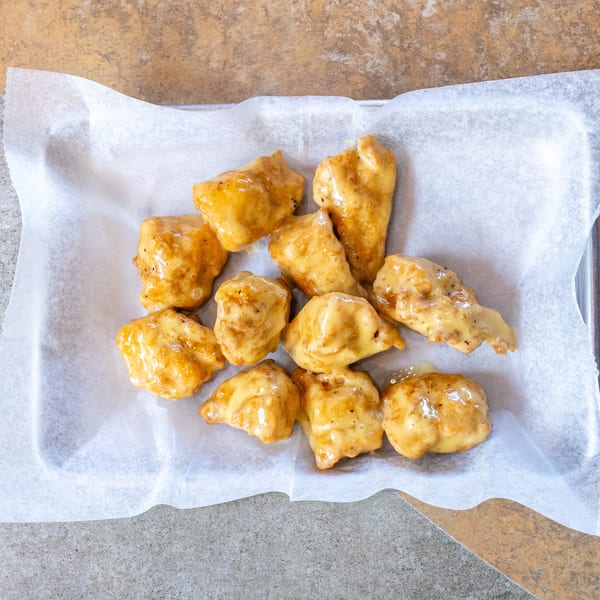 Ten boneless chicken wings coated in a creamy, golden sauce, served on white parchment paper.