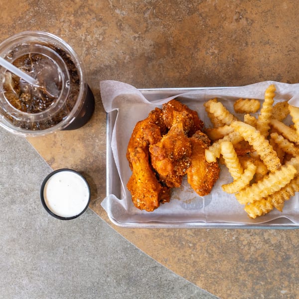 Top-down view of a meal with crispy chicken wings, crinkle-cut fries, a drink, and dipping sauce.