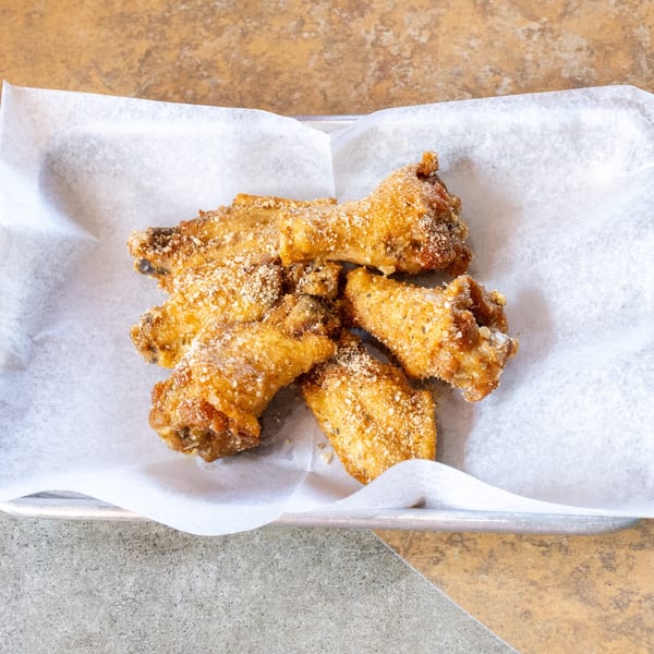 Crispy, golden-brown chicken wings dusted with parmesan cheese and herbs on white parchment paper.