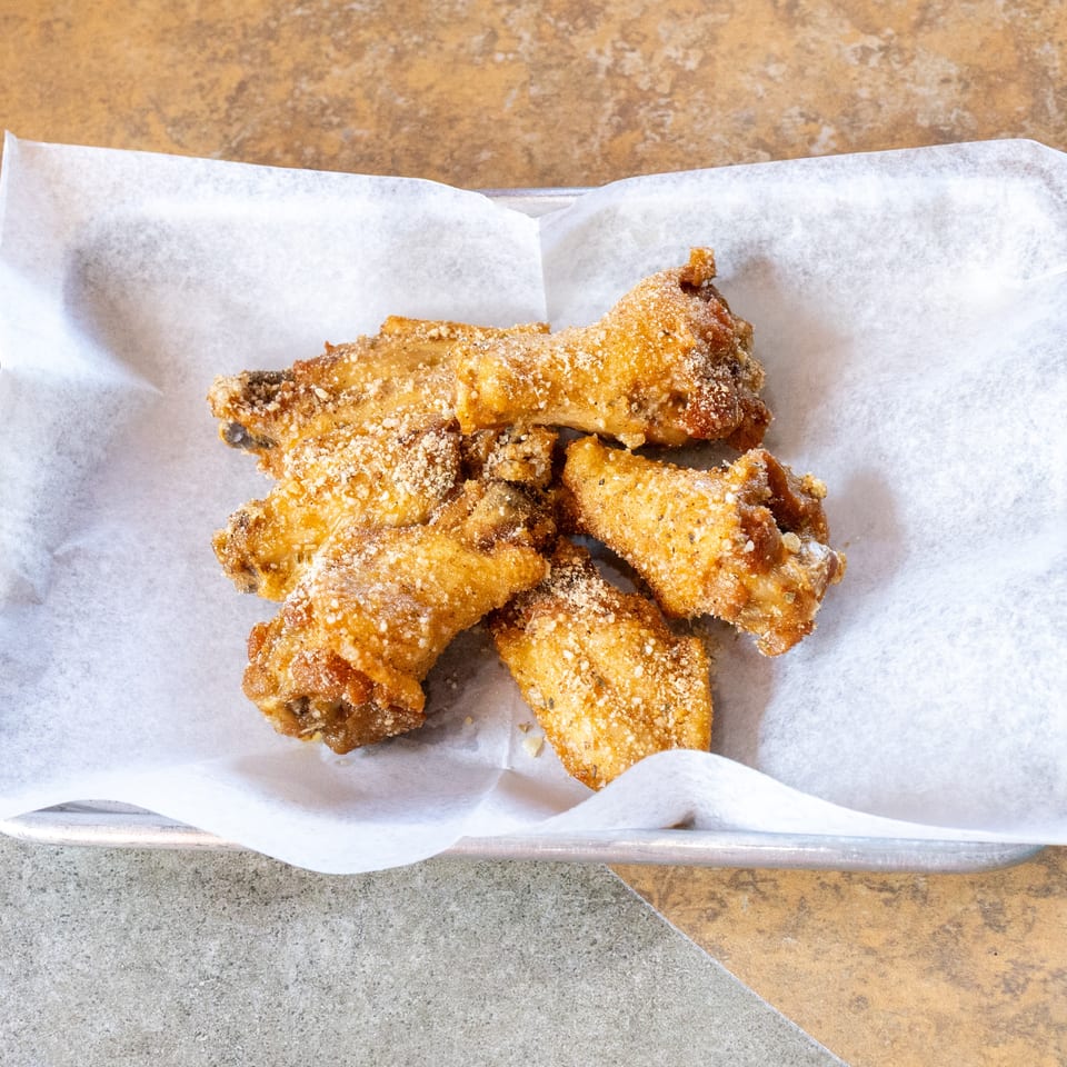 Crispy, golden-brown chicken wings dusted with parmesan cheese and herbs on white parchment paper.