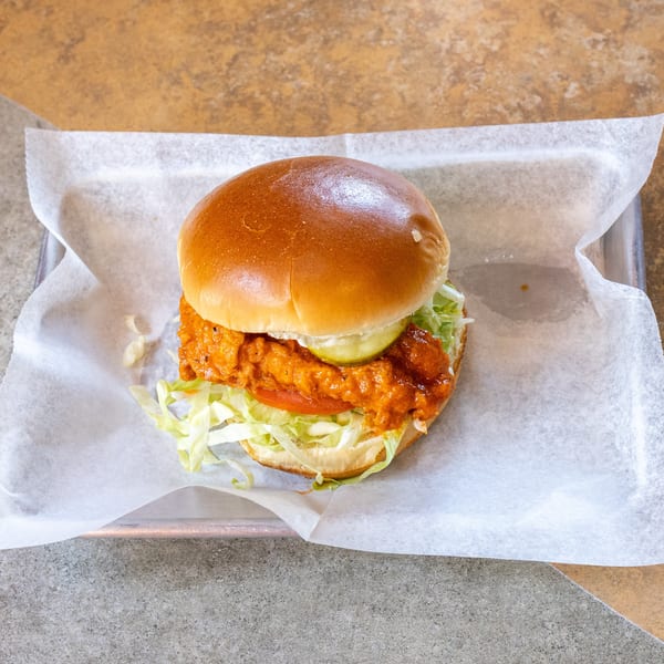 Spicy chicken sandwich with lettuce, tomato, and pickles on a bun, served on parchment paper.