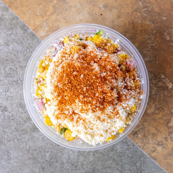 Overhead view of a plastic container filled with corn, cheese, and red spice.